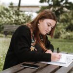 concentrated woman writing notes in papers in park