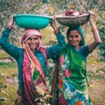two women wearing traditional dress carrying basins