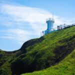 white concrete tower on green mountain under blue sky during daytime