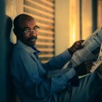 man in blue and white checkered dress shirt reading newspaper