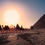 five persons riding camels walking on sand beside Pyramid of Egypt