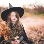 girl wearing black witch costume holding brown plant