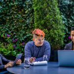 Three diverse adults engaging in an outdoor meeting with laptops and tablets in a garden.