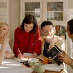 Group of young adults studying together at a kitchen table filled with books and notes.