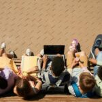 Group of teenagers sitting on a bench with a laptop, enjoying a sunny day outdoors.