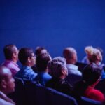 An attentive group of adults seated at an indoor conference, focusing on a presentation.