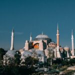 Famous Hagia Sophia grand mosque with high minarets and dome located among green trees in Turkey against blue sky in city