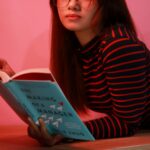 A woman lying on a pink background reading a book called 'The Making of a Manager'.