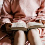 person reading book sitting on red and white striped bedspread
