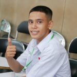 a young man sitting at a table giving a thumbs up