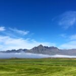 Stunning view of rocky mountains in Iceland with lush fields under a bright blue sky.