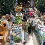 Vibrant indoor market scene with diverse people exploring fresh produce and handmade goods.