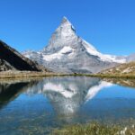 Breathtaking view of the Matterhorn mountain reflecting in a clear alpine lake under a bright blue sky.